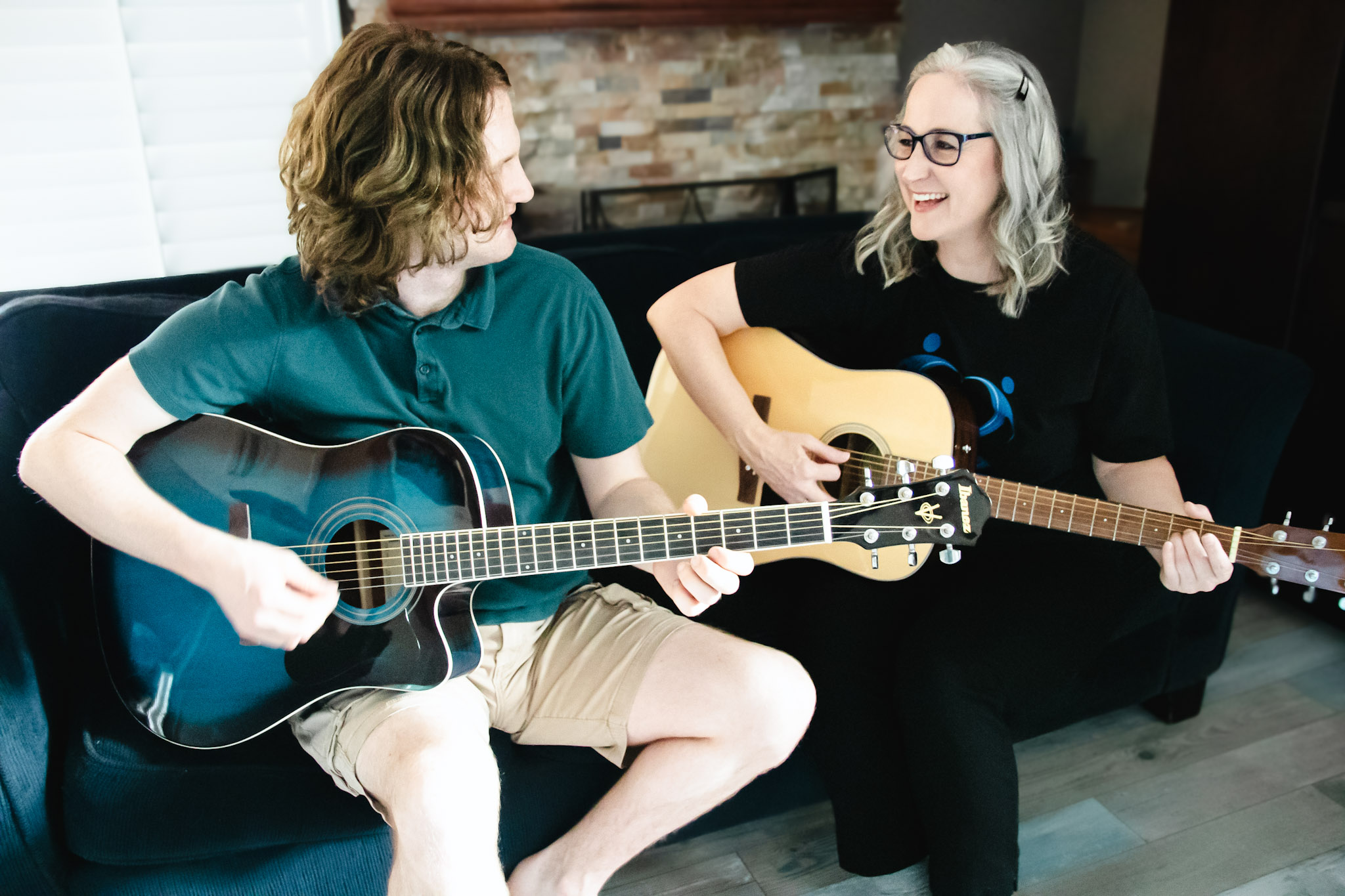 Jennifer and Jacob Swann playing acoustic guitars together on a couch.