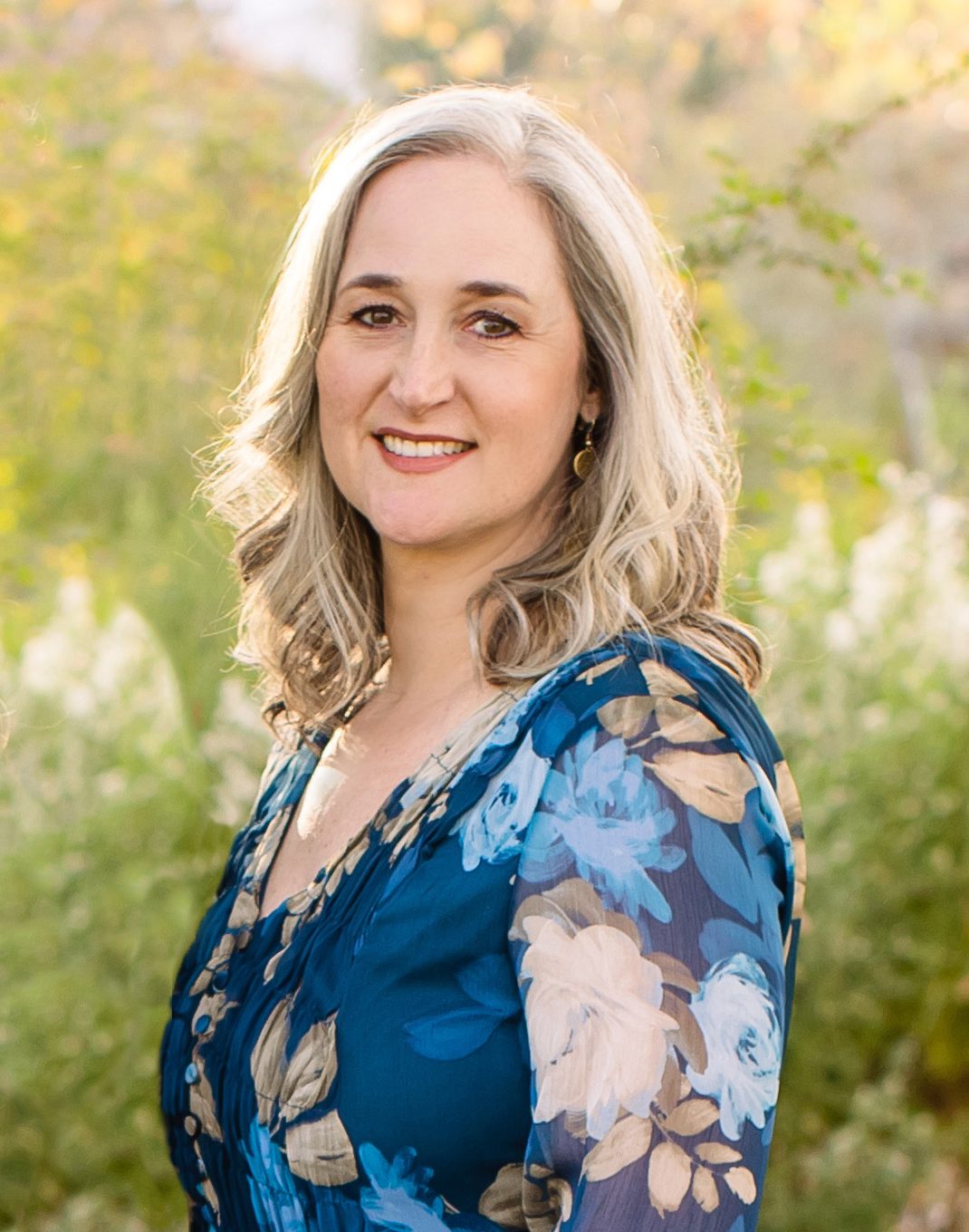 Jennifer Swann smiles with bushes and natural light in the backdrop.
