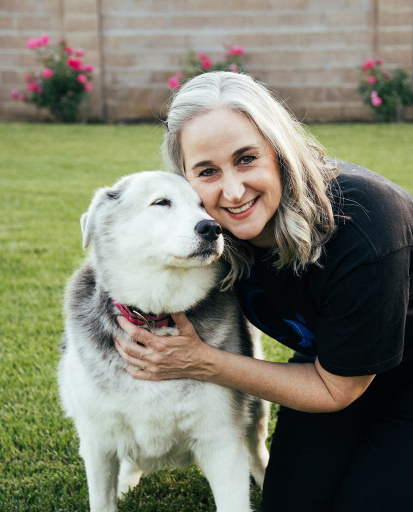 Jennifer Swann kneeling down in her lawn and embracing her dog, who appears relaxed and content.