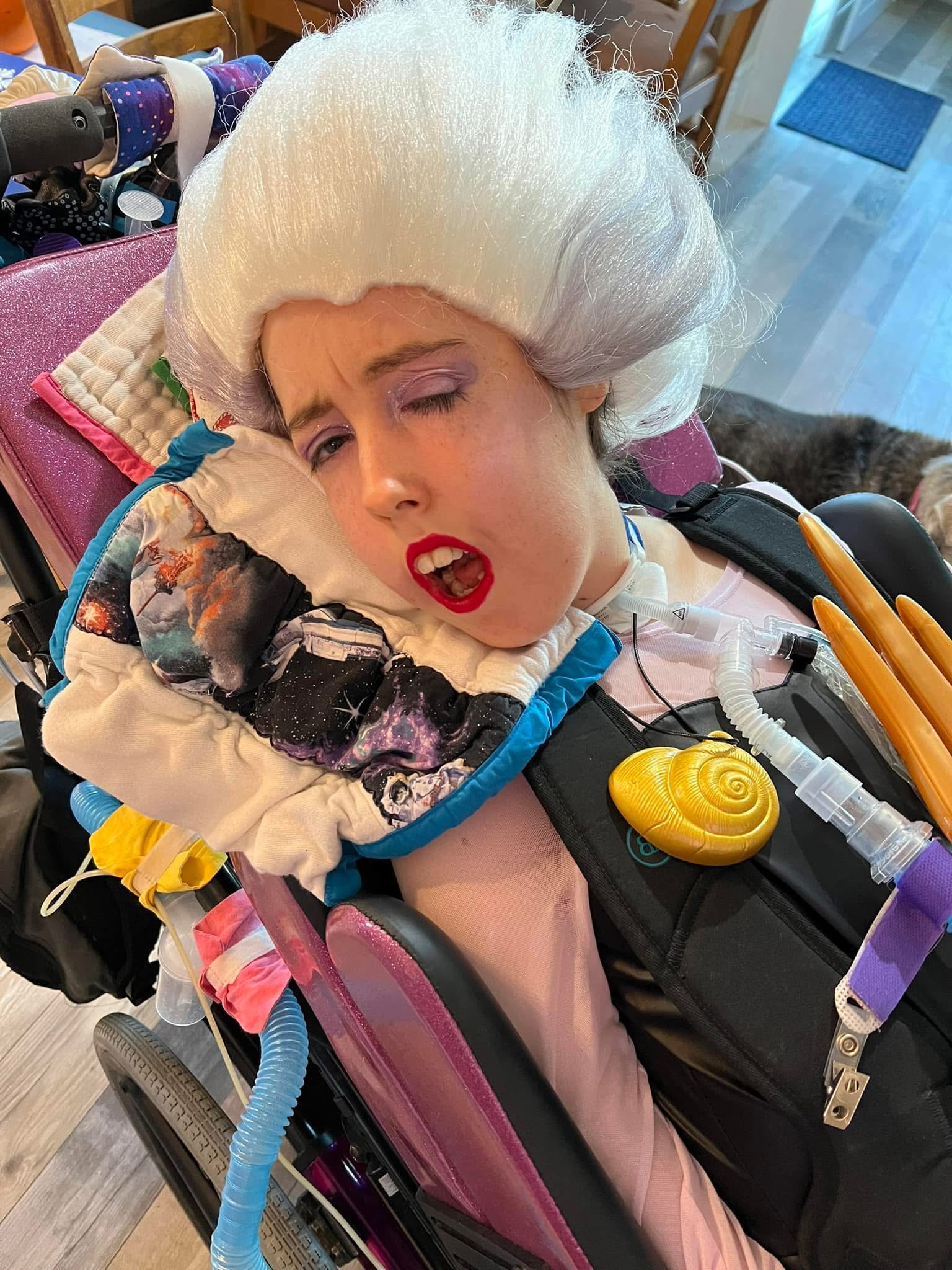 Kennedy in her wheelchair with makeup and a large white wig on.