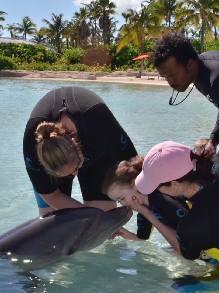 Kennedy at a tropical beach in the ocean, kissing a dolphin.