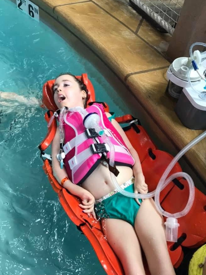 Kennedy floating in a pool, wearing a pink life preserver.