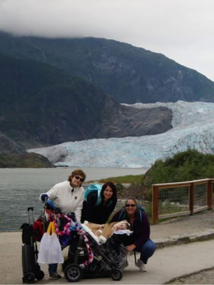 Jennifer, Kennedy, and two friends pose in front of a large glacier in Alaska.