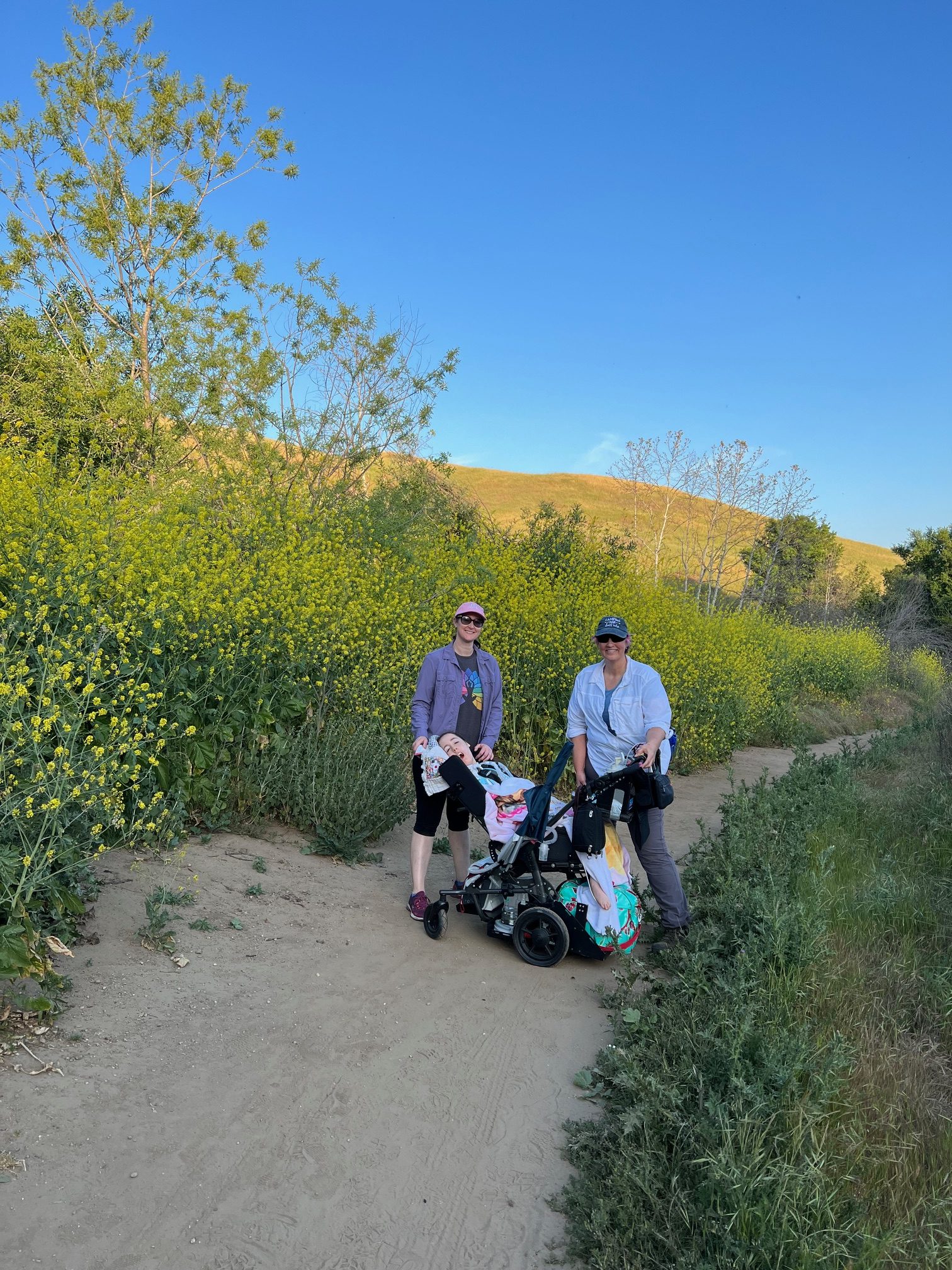 Kennedy, Jennifer, and a friend hiking on a dusty trail with clear blue skies behind them.